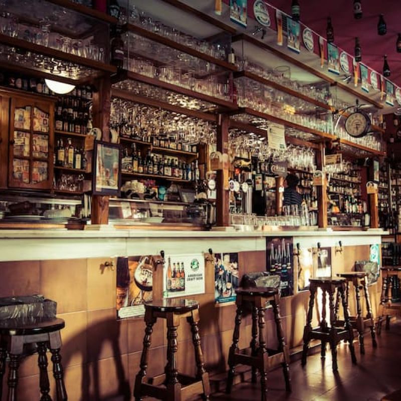 Dim pub interior with bar stools and shelves of glassware and bottles