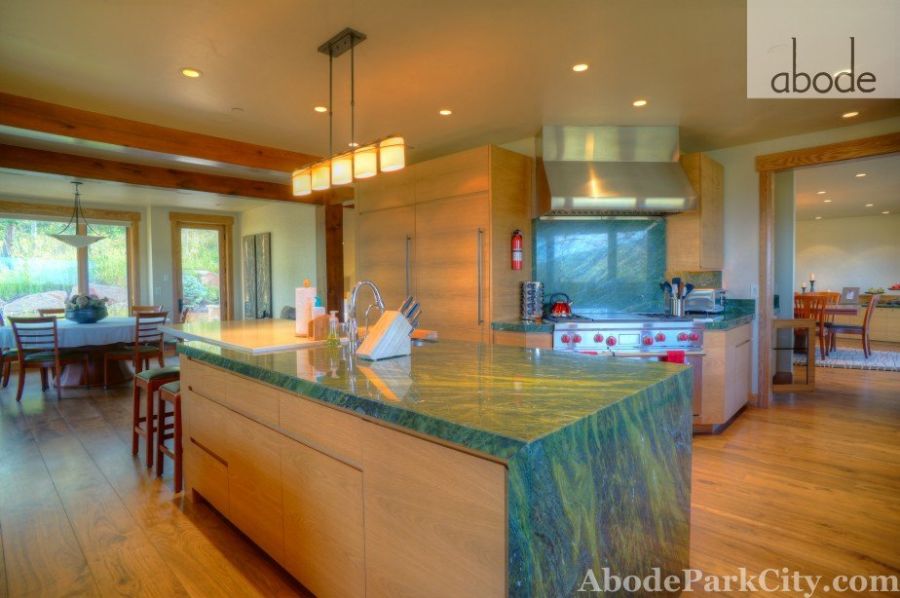 Modern kitchen with green stone island, wood cabinetry, and stainless range hood