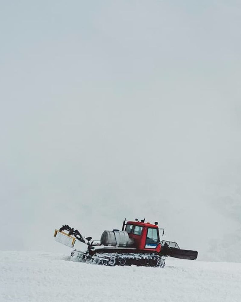 Red snowcat grooming machine driving across a fog-covered snowfield