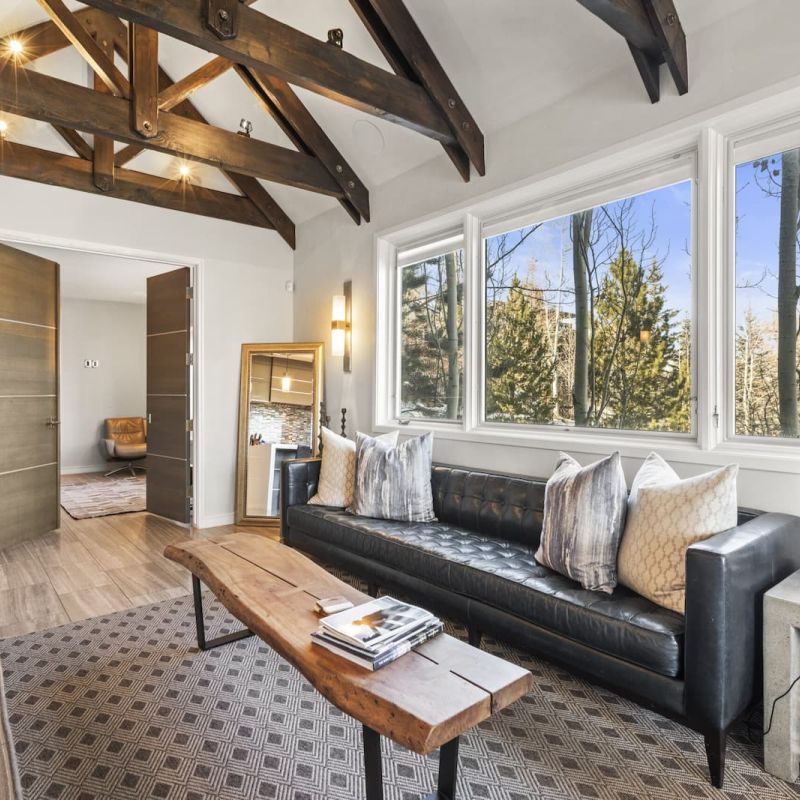 Living room with exposed wood trusses, leather sofa, and large picture windows