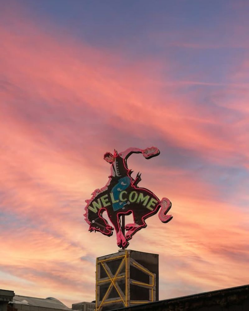 Neon bucking bronco welcome sign atop a building under a pink sunset sky