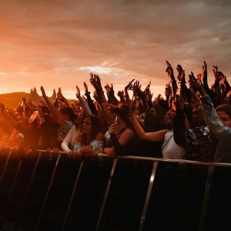 Concert crowd raising hands and phones at sunset behind a barricade