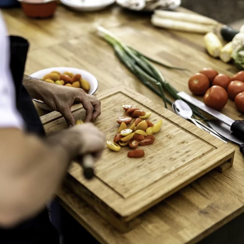 Chef slicing cherry tomatoes on a wooden cutting board with vegetables