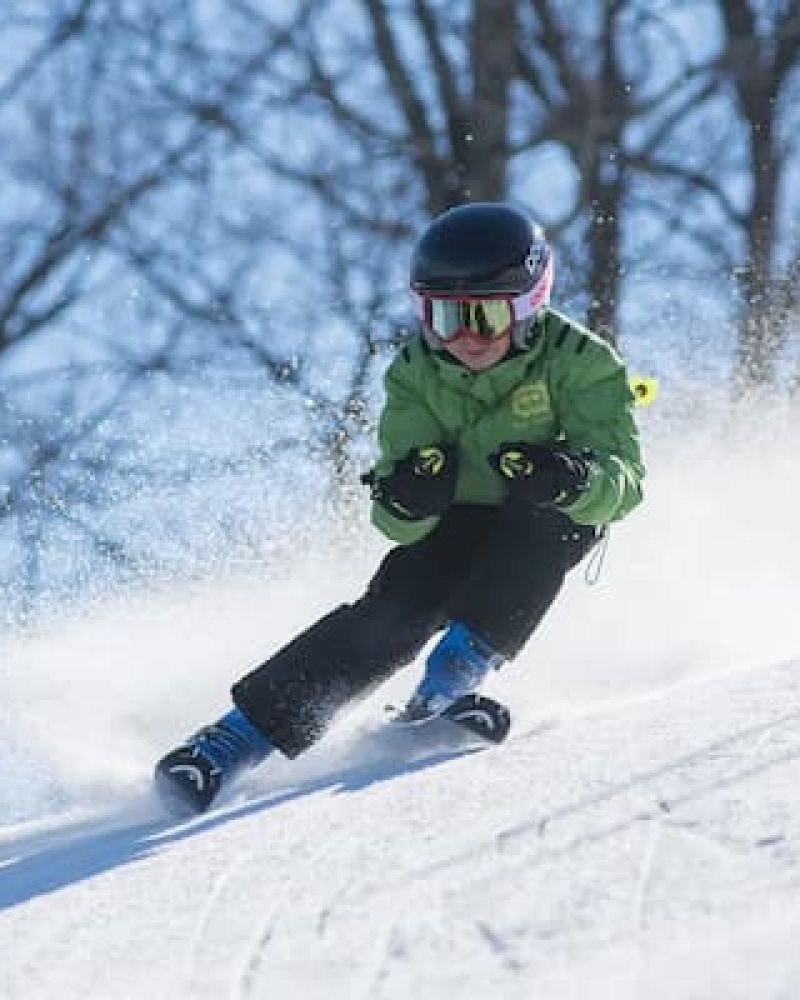 Young skier in green jacket carving a turn down a snowy slope
