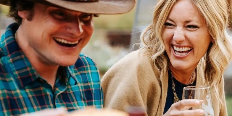 Man and woman in cowboy hat laughing together with white wine outdoors