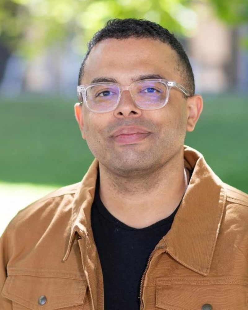 Headshot of a man with clear-frame glasses in a tan jacket