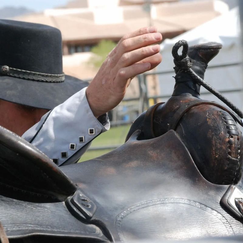 Cowboy in a black hat inspecting a leather western saddle