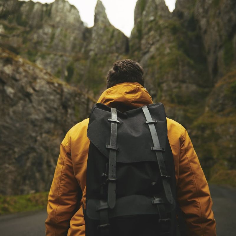 Hiker in yellow jacket and backpack walking toward jagged rocky cliffs