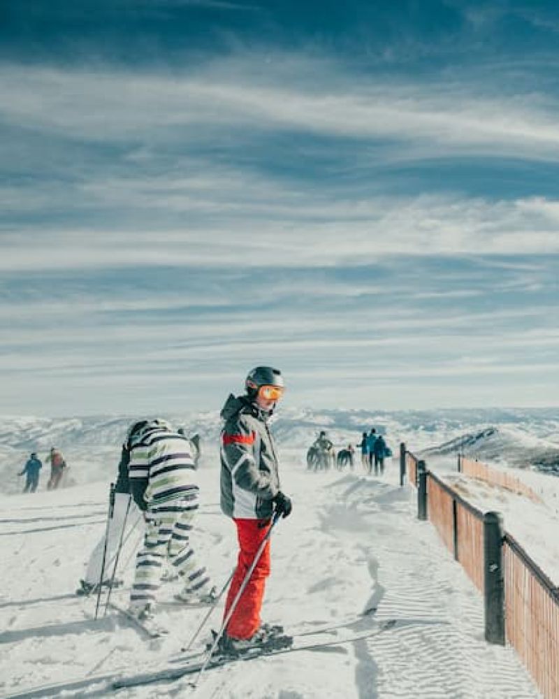 Skier in red pants standing at a mountaintop fence with valley views