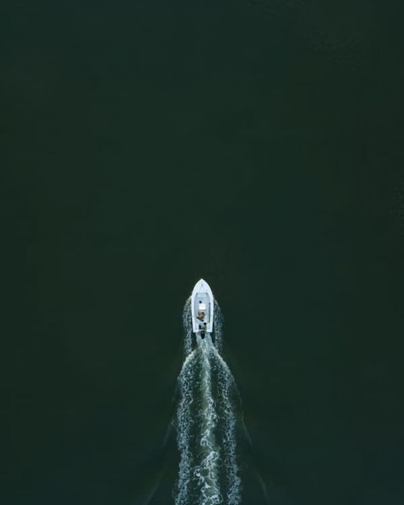 Aerial view of a small white motorboat carving a wake across dark green water