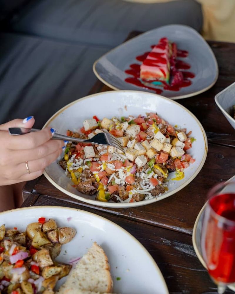 Plate of breakfast hash with tomato and cheese being eaten alongside cheesecake and rose