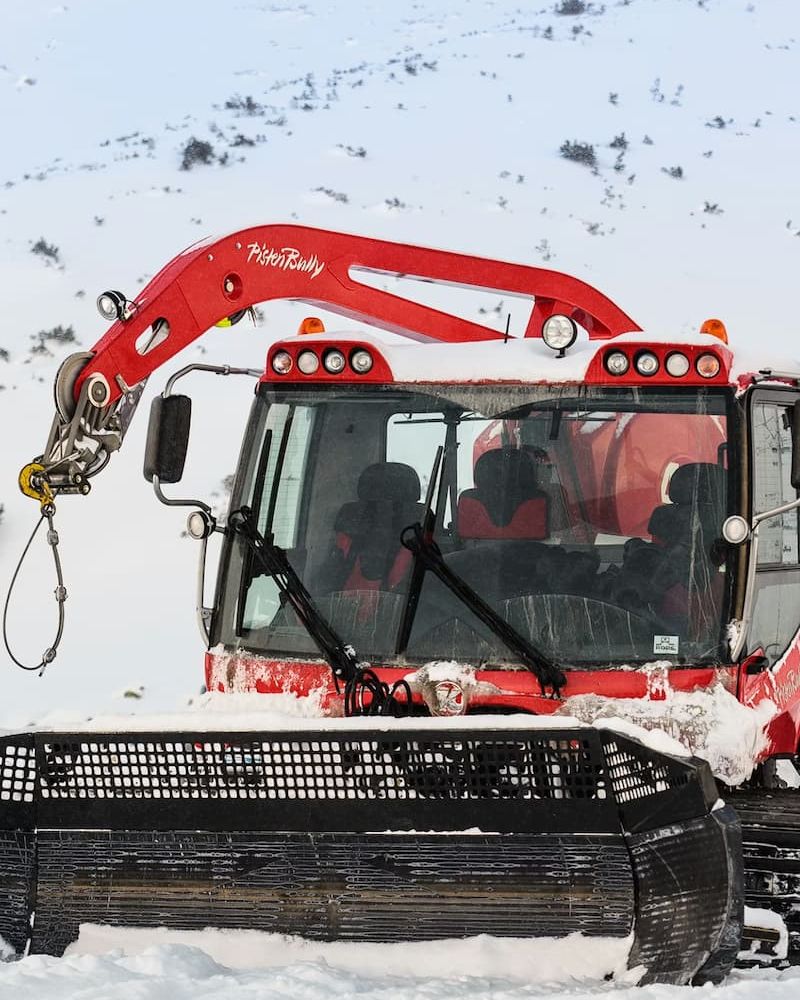 Red PistenBully snowcat with passenger cabin parked on a snowy slope