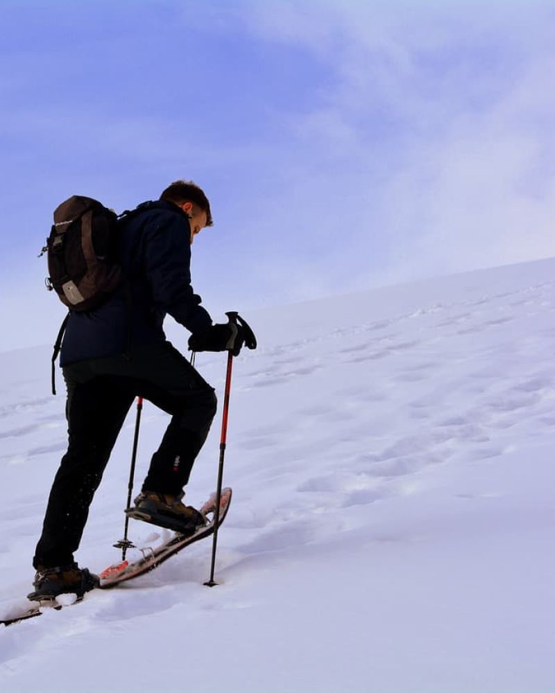 Snowshoer with poles and backpack climbing a snowy slope