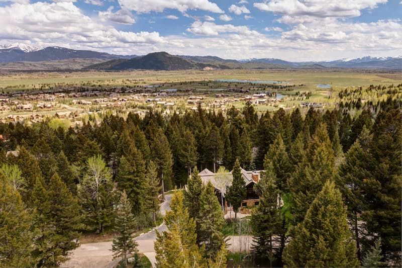 Aerial view of a timber home tucked among pines with mountain valley beyond