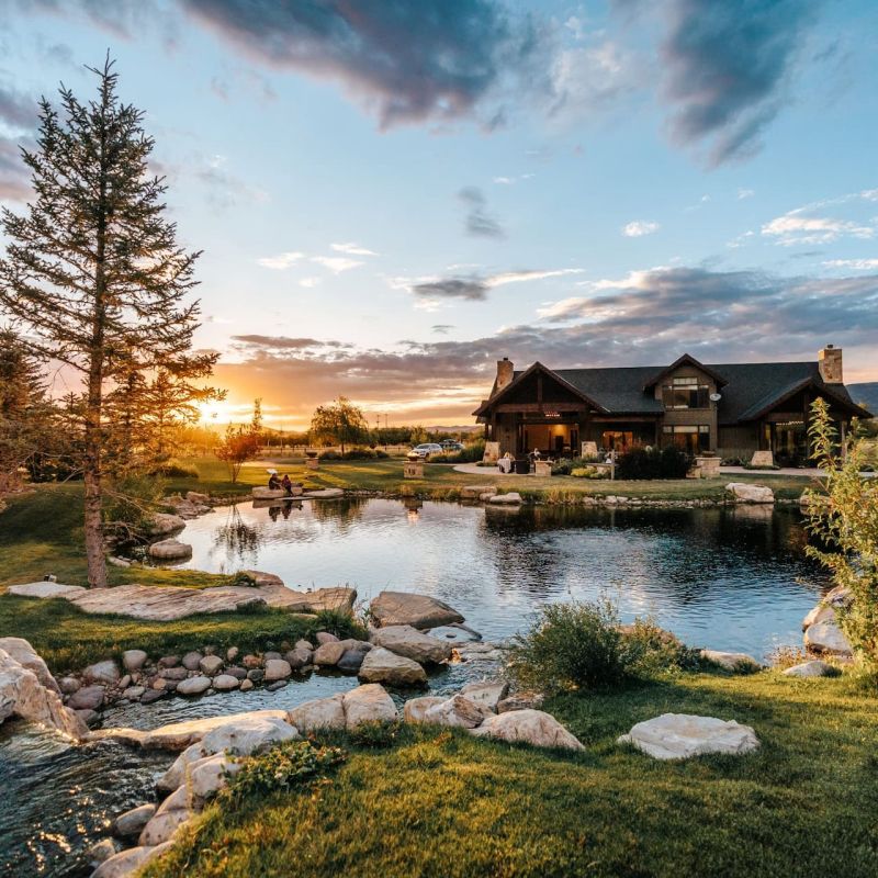 Mountain home at sunset reflected in a landscaped pond with stone-lined stream