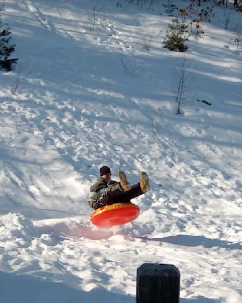 Person catching air on an orange snow tube on a sunlit slope