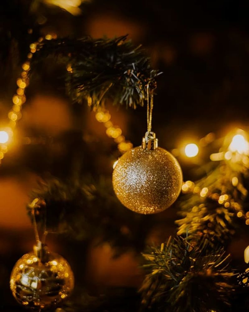 Glittering gold ornament hanging on a lit Christmas tree