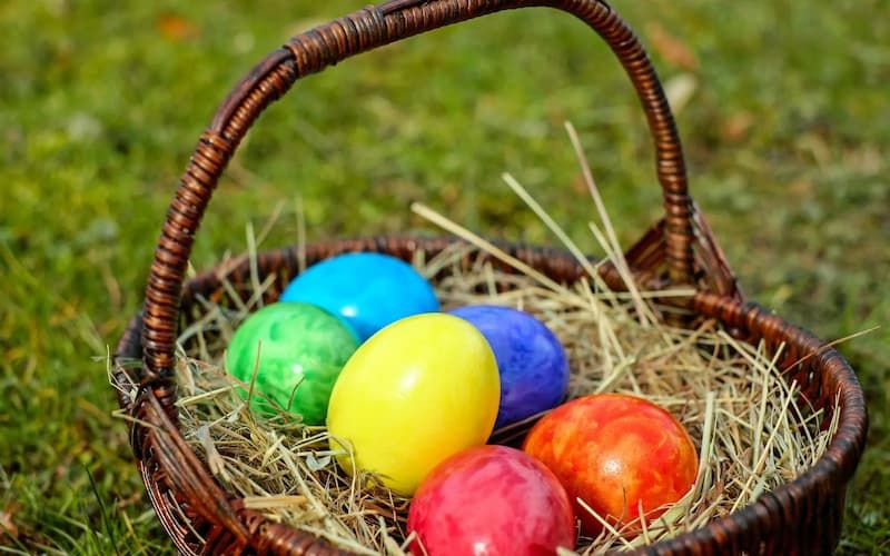 Wicker basket holding six dyed Easter eggs in the grass