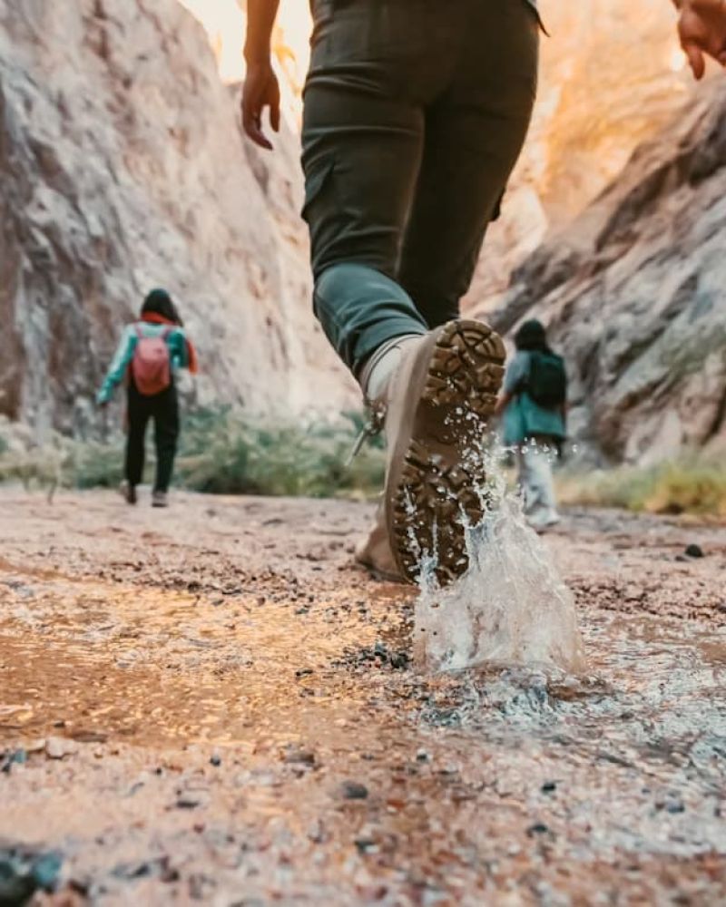 Close-up of a hiker's boot splashing through a stream in a desert canyon