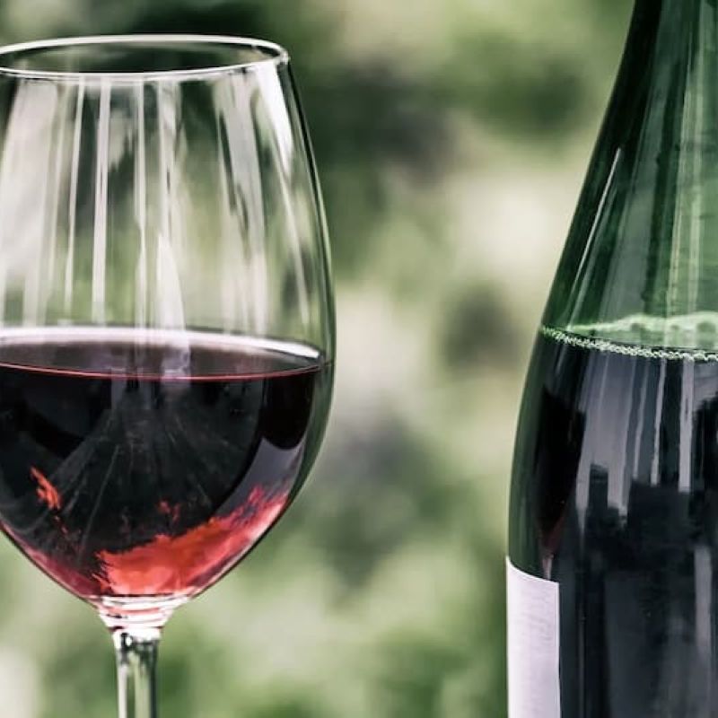 Glass of red wine beside a dark wine bottle on a garden table