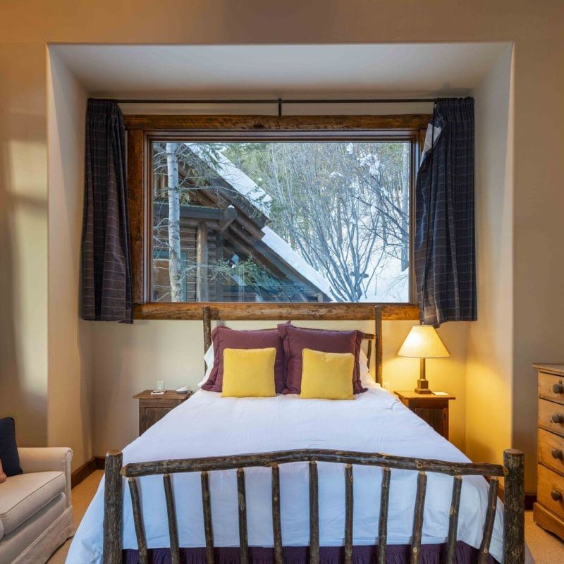 Bedroom with rustic log bed frame and window overlooking snowy trees