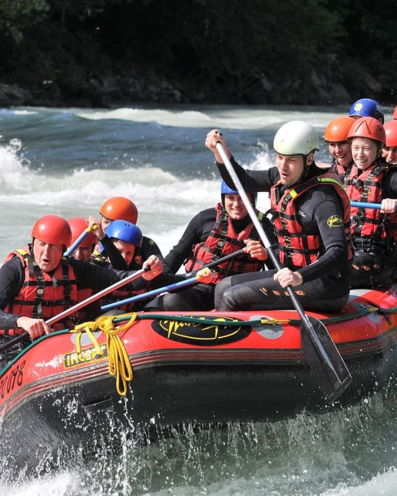 Group whitewater rafting through rapids in a red raft with paddles raised