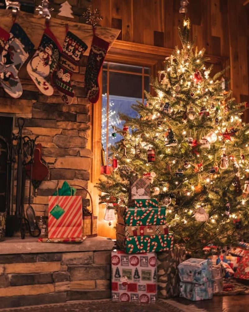 Stone fireplace with hung stockings beside a lit Christmas tree and wrapped gifts