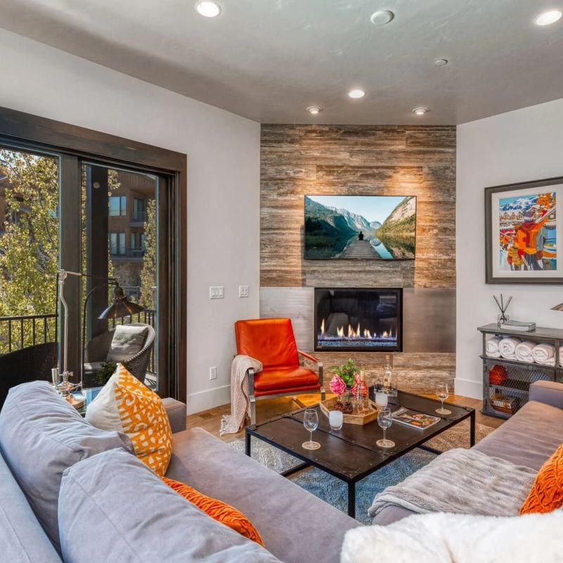 Modern living room with gray sectional, orange accents, mounted TV above linear fireplace