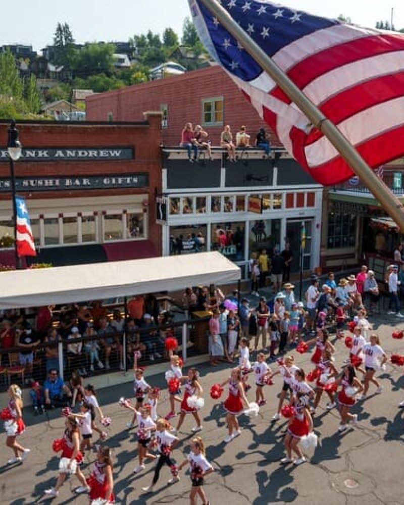 American flag flying over a Main Street parade with cheerleaders marching