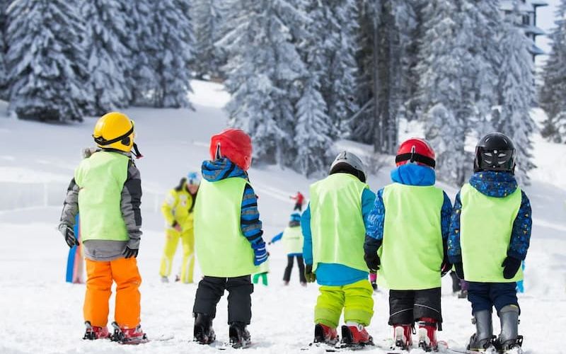 Group of children in green vests on skis at a learn-to-ski lesson