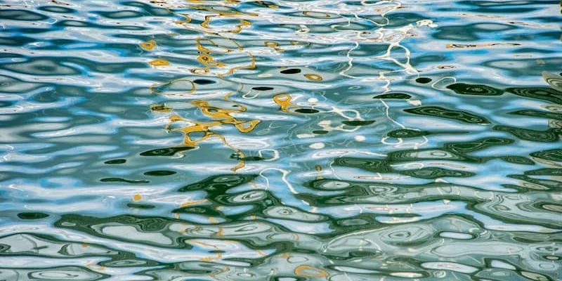 Close-up of rippling water surface with green and yellow reflections