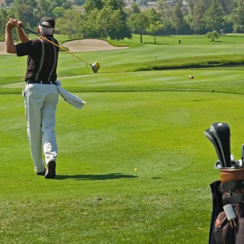 Golfer following through on a tee shot with bag of clubs in foreground