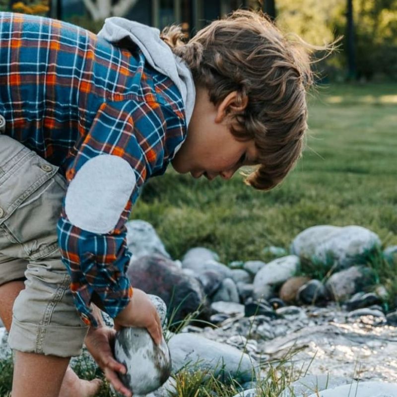 Boy in flannel shirt picking up a stone beside a backyard creek bed
