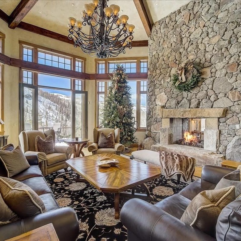 Great room with stone fireplace, leather sofas, vaulted timber ceiling, and mountain windows
