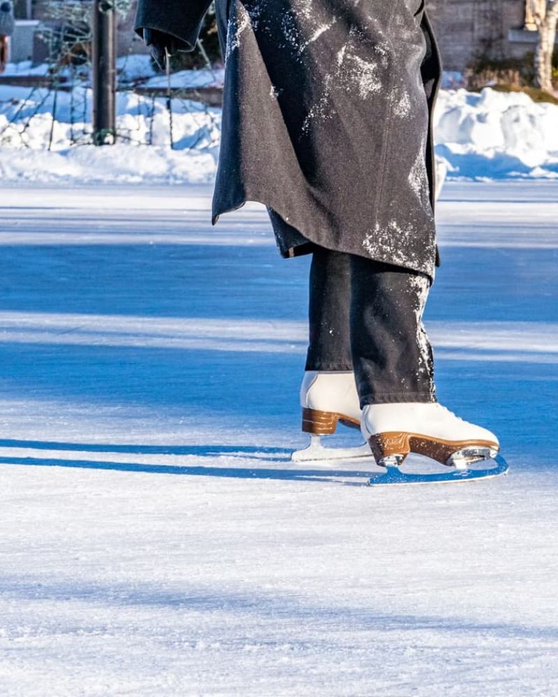 Skater in white figure skates gliding across a sunlit outdoor rink