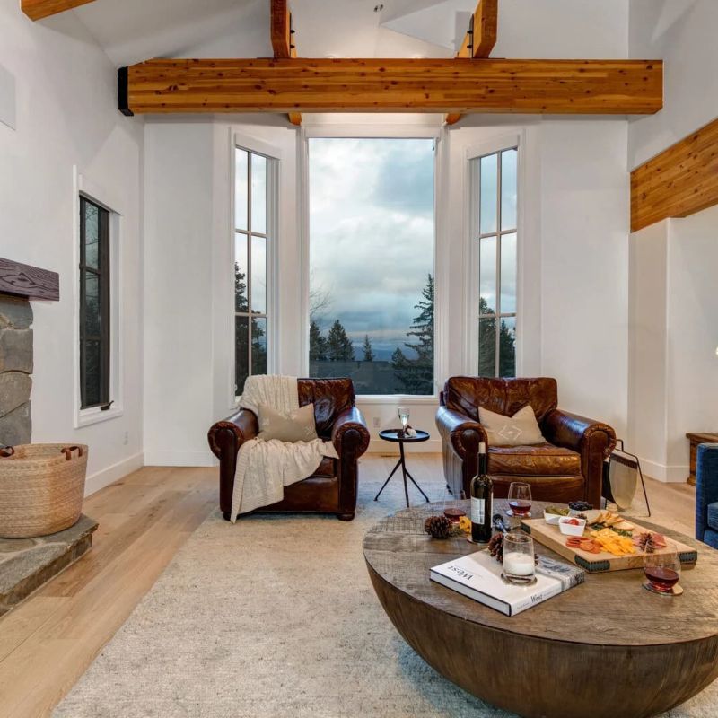Living room with stone fireplace, leather chairs, and vaulted ceiling windows
