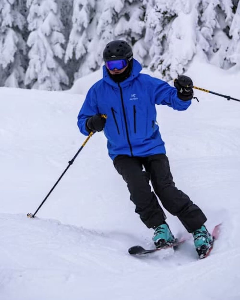 Skier in blue jacket carving down a snowy run beside frosted evergreens