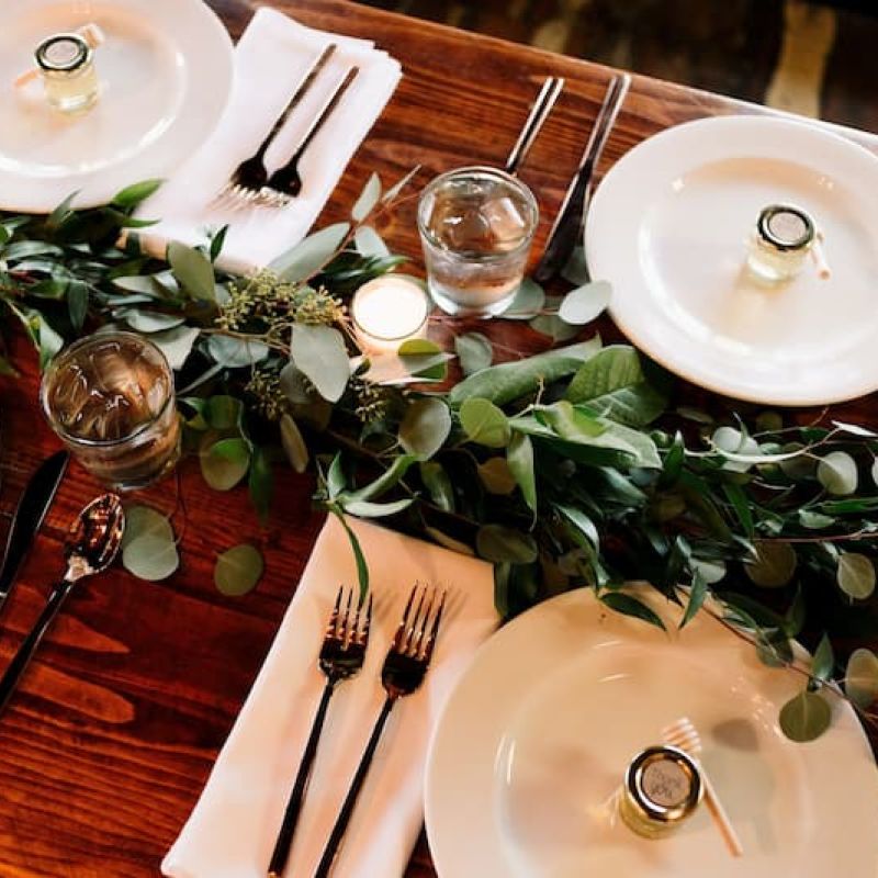 Long farmhouse dining table set with white plates, candles, and a eucalyptus garland runner