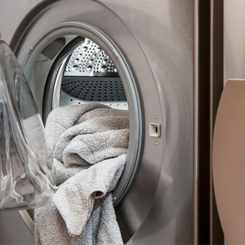 Open front-load washer with a folded towel inside next to a dryer
