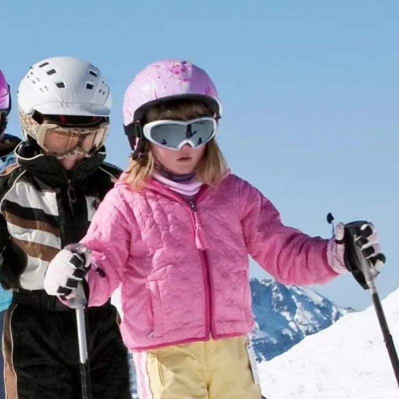 Group of helmeted children skiing downhill behind their instructor
