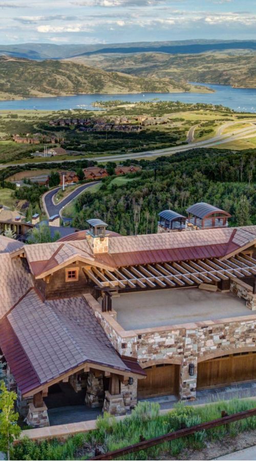 Aerial view of a stone-and-timber luxury home overlooking a mountain reservoir near Park City, Utah