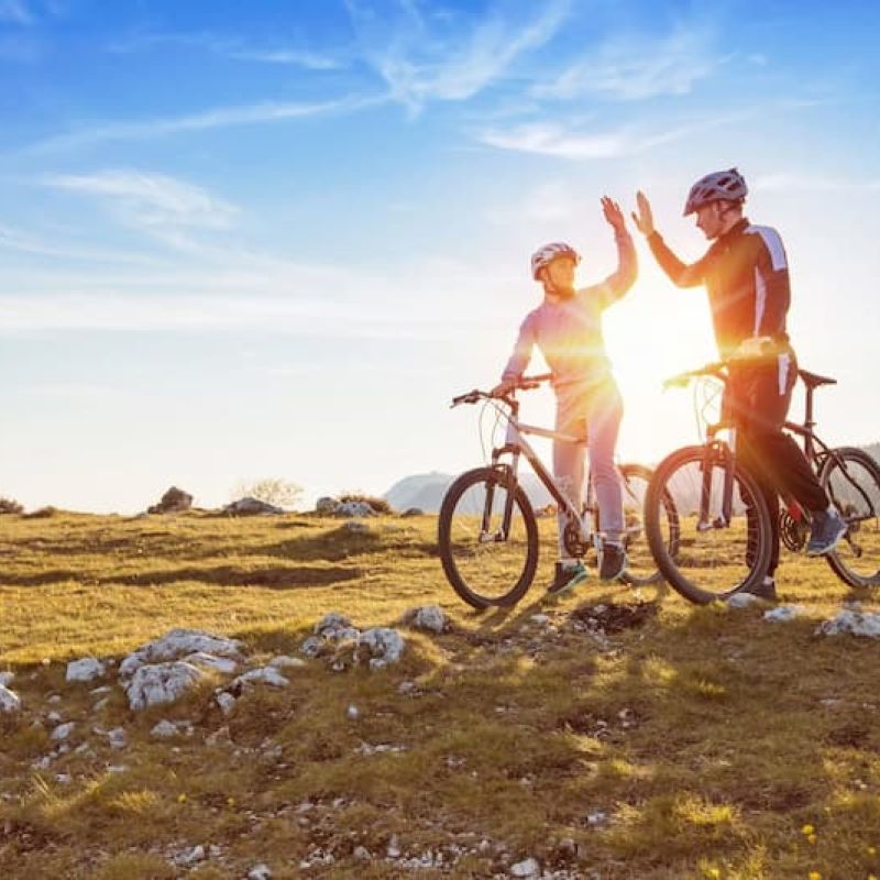 Two cyclists high-fiving on mountain bikes at sunset on an open ridge