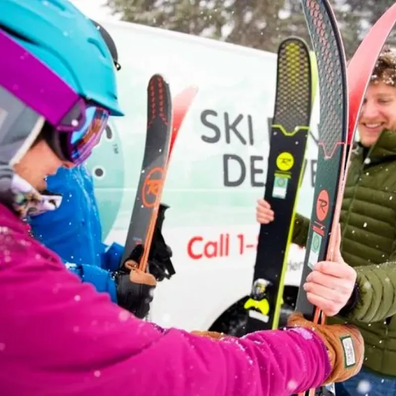 Skiers receiving rental skis from a Ski Butlers delivery van in the snow