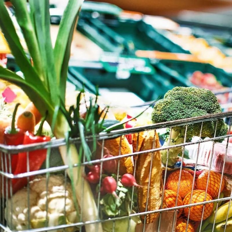 Grocery cart filled with fresh produce in a supermarket aisle