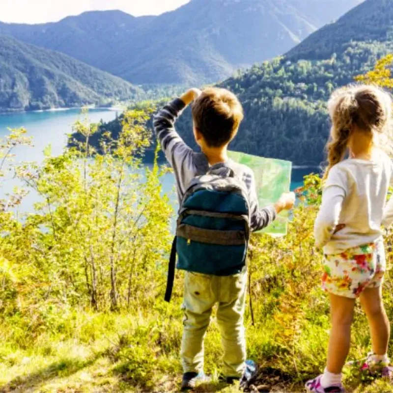 Two children with a backpack pointing at a map above a mountain lake