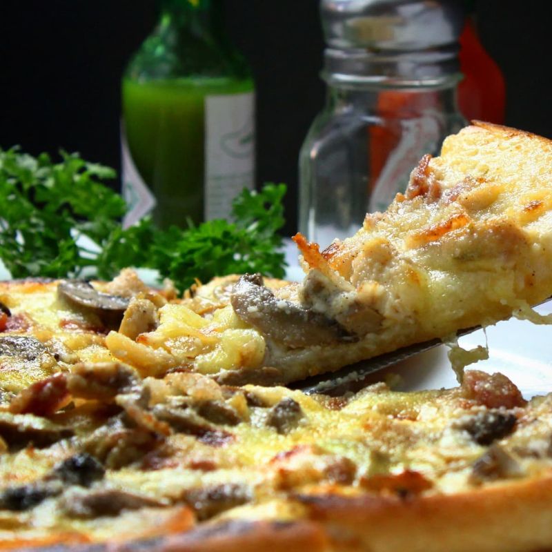 Slice of mushroom and cheese pizza being lifted from a whole pie