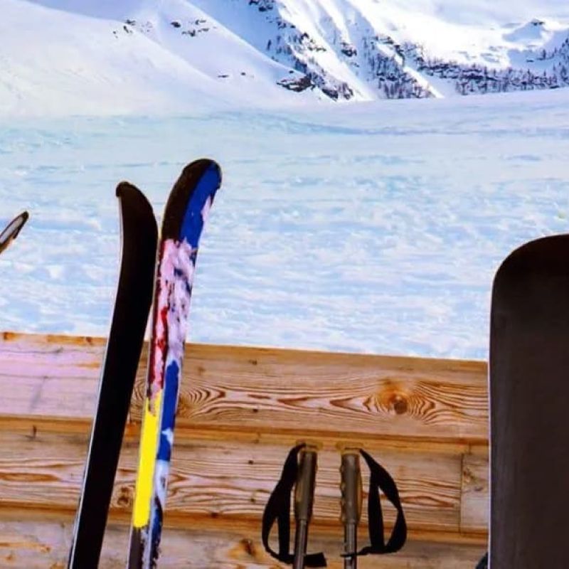 Row of skis, poles, and a snowboard leaning against a wooden rack