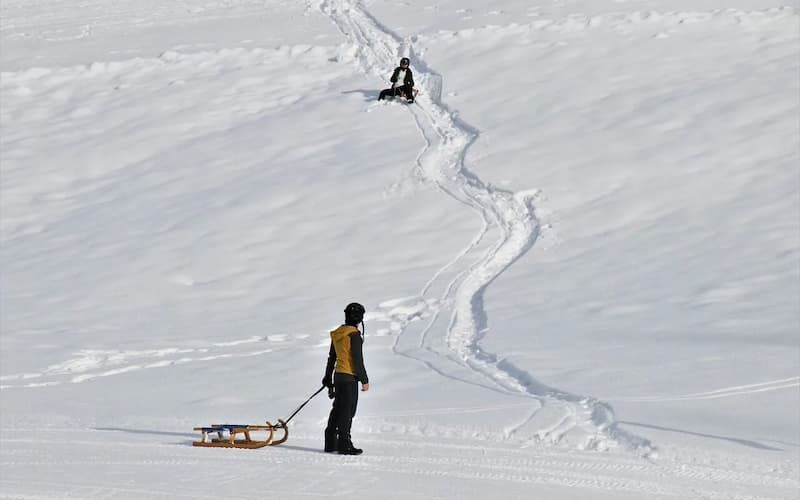 Two people pulling sleds across a wide open snowfield