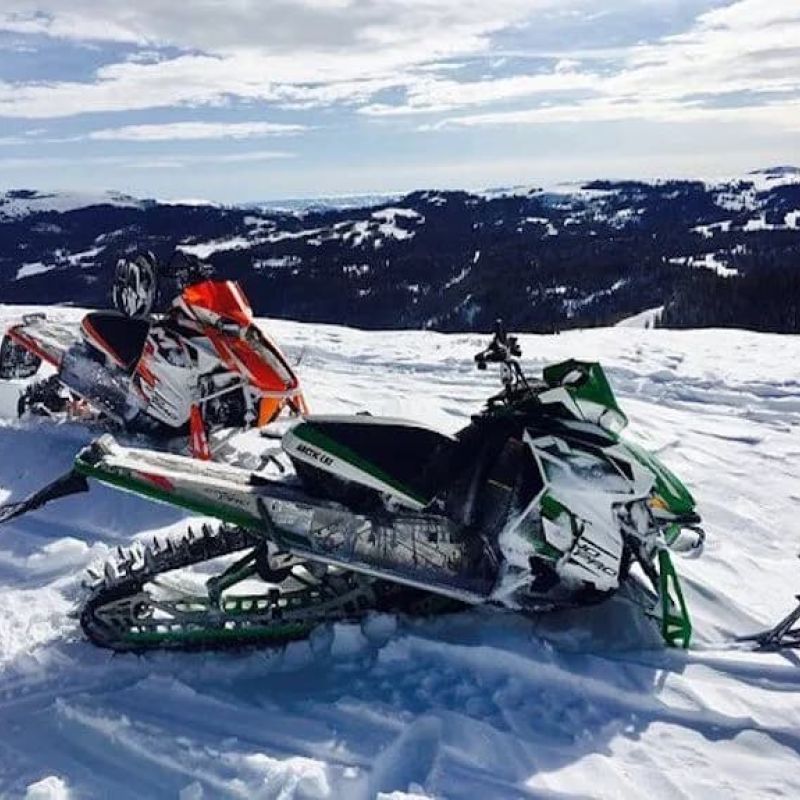 Two snowmobiles parked on a snowy mountain ridge