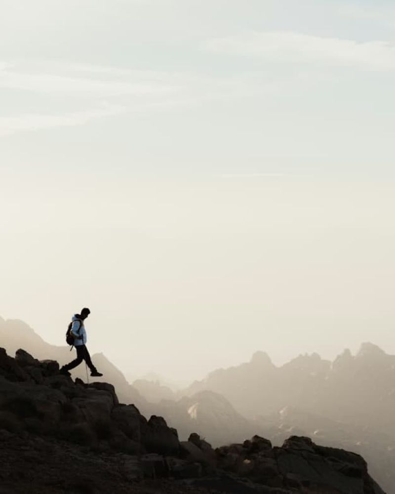 Hiker silhouetted on a rocky ridgeline at dusk with hazy peaks behind